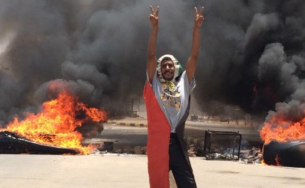 A protester flashes the victory sign in front of burning tires and debris near Sudan's military headquarters. For months demonstrators have been demanding a a transition to civilian rule. A protester flashes the victory sign in front of burning tires and debris near Sudan's military headquarters. For months demonstrators have been demanding a a transition to civilian rule.