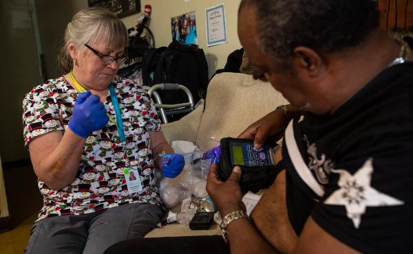 Arthur Jackson (right) gets blood tests during home visits in Boston from nurse Brenda Mastricola. He's also getting intravenous penicillin to treat a serious bone infection in his foot. The medication's pump is connected to an indwelling IV catheter. It' Arthur Jackson (right) gets blood tests during home visits in Boston from nurse Brenda Mastricola. He's also getting intravenous penicillin to treat a serious bone infection in his foot. The medication's pump is connected to an indwelling IV catheter. It'