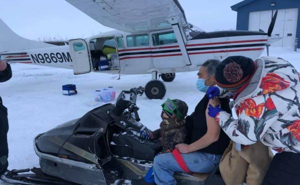 Sarah Lind, a nurse with Yukon-Kuskokwim Health Corp., Southwest Alaska's tribal health care provider, vaccinates James Evan in December. They're standing on the tarmac in the village of Napakiak, where Evan works for YKHC at the clinic. Sarah Lind, a nurse with Yukon-Kuskokwim Health Corp., Southwest Alaska's tribal health care provider, vaccinates James Evan in December. They're standing on the tarmac in the village of Napakiak, where Evan works for YKHC at the clinic.
